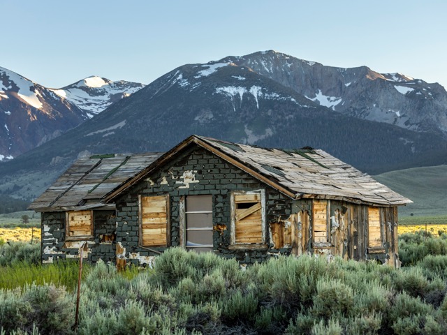 A weathered wooden cabin below a mountain range