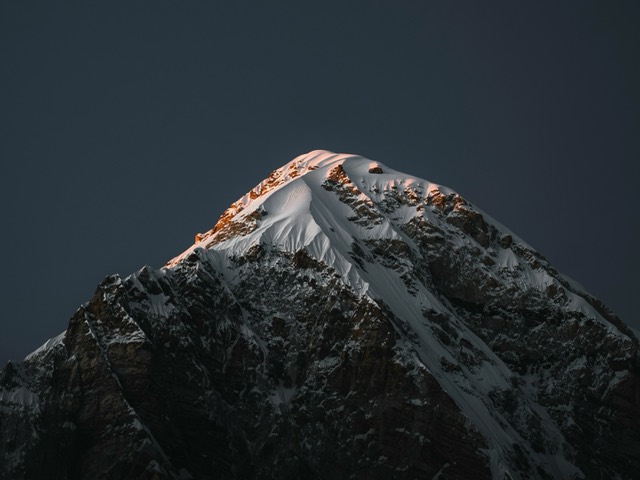 A snow-covered mountain peak rising from deep shadow