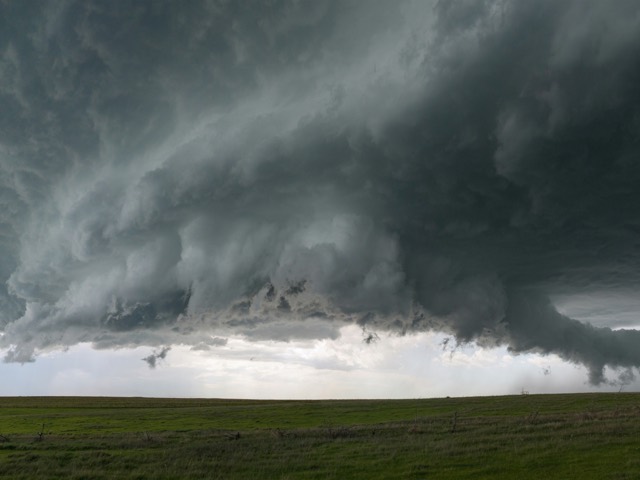 A tornado descending from dark storm clouds over open grassland