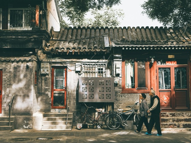 Cyclists and pedestrians passing historic Beijing courtyard architecture